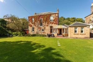 an old brick house with a grass yard at Burnock Lodge with Hot Tub in Ayr