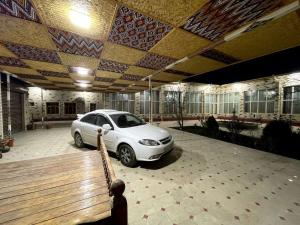 un coche blanco aparcado en un estacionamiento con un banco en Shukrona Guest house, en Bukhara
