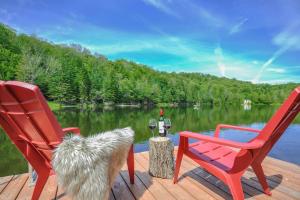 two red chairs and a table with wine glasses on a dock at Chalet du Domaine Spa privé et lac in Saint Adolphe D'Howard
