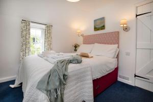 a bedroom with a bed with white sheets and a window at Lavender Cottage in Porthscatho
