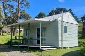 a small white tiny house with a porch at Pukenui Holiday Park in Pukenui