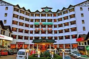 ein großes weißes Gebäude mit Autos auf einem Parkplatz in der Unterkunft Hotel Rosa Passadena in Cameron Highlands