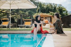 two women sitting next to a swimming pool drinking wine at B&B Toblerina in Ascona