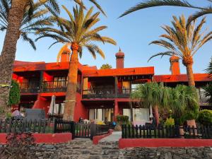 a red building with palm trees in front of it at Vivienda Vacacional frente al mar Playa del Aguila in Playa del Aguila