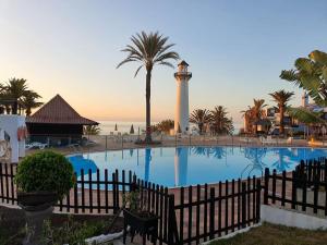 a pool with a lighthouse and palm trees and a fence at Vivienda Vacacional frente al mar Playa del Aguila in Playa del Aguila
