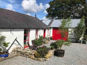a white building with a red door and some plants at Stone Wall Cottage in Castlewellan