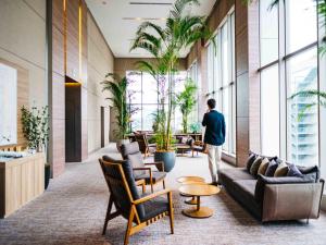 a man standing in a lobby with furniture and plants at Hotel Resol Trinity Hakata in Fukuoka
