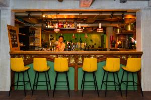 a man standing behind a bar with yellow bar stools at The Barthels Boutique Hotel in Würzburg
