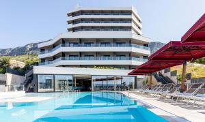 a hotel with a swimming pool and red umbrellas at Hotel Plaža Duće in Duće