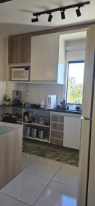 a kitchen with white cabinets and a large window at Apartamento Confortável Inteligente in Poços de Caldas