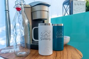 a coffee maker and two cups on a wooden table at Timberline Glamping Orange Beach in Gulf Shores