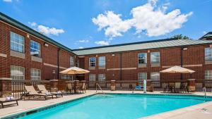 a pool with chairs and umbrellas in front of a brick building at Best Western Plus Addison/Dallas Hotel in Addison