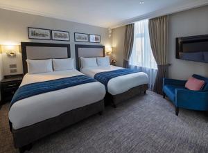 a hotel room with two beds and a blue chair at Wellington Hotel by Blue Orchid in London