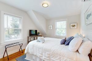 a bedroom with a white bed and two windows at Oyster Beach Bungalow in Chatham