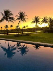 a pool with palm trees and a sunset in the background at Praia do Forte Iberostar in Praia do Forte