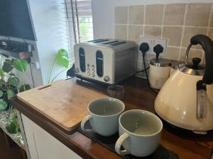 a counter with two cups and a toaster on a kitchen counter at Harlequin Cottage in Llangernyw