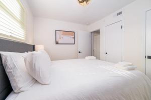 a white bedroom with a large bed with white pillows at Sojourn's Harborage Pelican Suite in North Camellia Acres