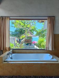 eine Badewanne in einem Raum mit einem großen Fenster in der Unterkunft Putra'Lebah Amed Guest House in Amed