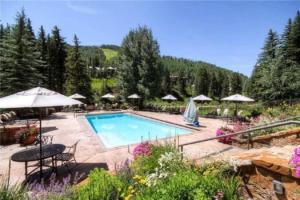 a swimming pool with chairs and umbrellas in a garden at Ski In, Ski Out 2 Bedroom Vacation Rental In The Heart Of Lionshead Village With Heated Slope Side Pool And Hot Tub in Vail