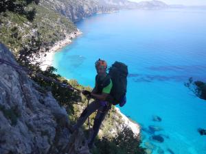 a man with a backpack standing on a cliff near the ocean at Hotel Bia Maore in Baunei