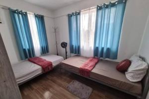 two beds in a room with blue curtains at BacolodCrib in Bacolod