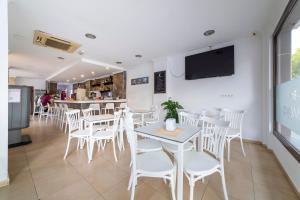 Un restaurante con mesas y sillas blancas y un televisor en la pared. en Hostal Moya, en Roquetas de Mar
