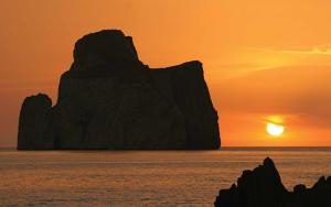 a sunset over a large rock formation in the ocean at Villaggio Malfidano in Buggerru
