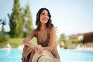 a woman in a bikini sitting next to a swimming pool at Hunguest Hotel Pelion in Tapolca