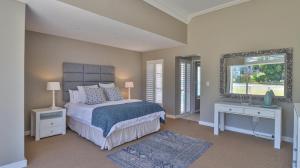a bedroom with a bed and two tables and a mirror at House Susan Pardew Hersham in Great Brak River
