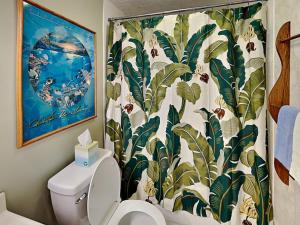 a bathroom with a toilet with a tropical shower curtain at Menehune Shores 206 in Kihei +14 photos