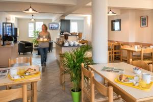 a woman walking through a restaurant with tables and chairs at Brit Hotel Essentiel Deltour Mende in Mende