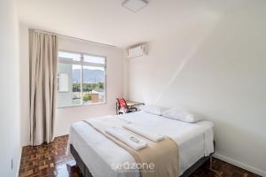 um quarto branco com uma cama e uma janela em Apartamento Aconchegante Bem Localizado RBE0031 em Florianópolis