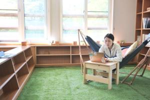 a woman sitting in a hammock using a laptop at ペコレラ学舎 Pekolela YAKUMO in Yakumo