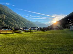 a green field with the sun setting in the mountains at TYROL PURElife Lodges in Sankt Jakob in Defereggen +38 photos