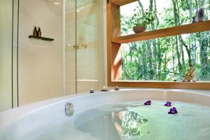 une baignoire avec des fleurs violettes et une fenêtre dans l'établissement Chalé Ametista com ofurô e lareira, Santo Antônio do Pinhal, à Santo Antônio do Pinhal