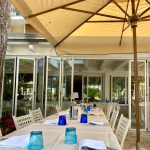 a long table with white chairs and a umbrella at Hotel Franca in Milano Marittima