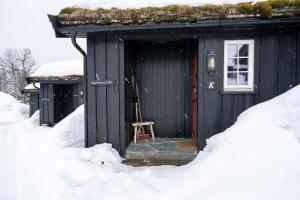 a black cabin with a wooden door in the snow at Bitigrenda K in Beitostøl