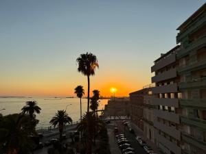 Una puesta de sol sobre el océano con una palmera y un edificio. en Ai Marinai Maestrale Apartment, en Taranto