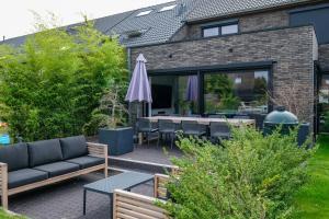 eine Terrasse mit einem Sofa, Tischen und einem Sonnenschirm in der Unterkunft Spacious family home 10 min from downtown Ghent in Gent