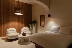 a bedroom with a white bed and two chairs at Narrativ Lofts in Campeche