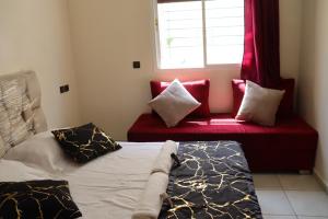 een slaapkamer met een bed en een raam en een rode bank bij Al-Sabah Residence Agadir in Agadir
