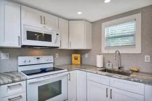 eine Küche mit weißen Schränken, einem Herd und einer Mikrowelle in der Unterkunft Coastal Cottage - Just 7 Minutes to the Beach and Downtown! in Lake Worth