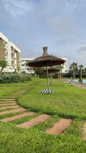 Appartement avec piscine à casa tamaris في دار بوعزة: مظلة من القش موضوعة فوق حقل عشبي