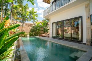 a swimming pool in front of a house with palm trees at Villa GMT Canggu - By Bali Lyfe Venture in Canggu