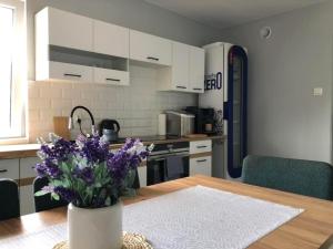 a kitchen with a table with purple flowers in a vase at Apartamenty przy Skwerku in Sztutowo