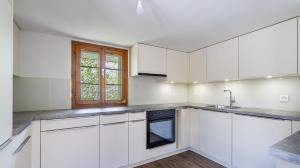 an empty kitchen with white cabinets and a window at Gästehaus Lindenplatz in Gunzwil