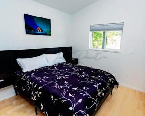 a bedroom with a bed with a purple comforter and a window at LuxQuarters Bumbleberry Guest House in Kitimat