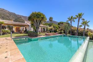 a swimming pool in front of a house with palm trees at Finca Lechuza in Mijas