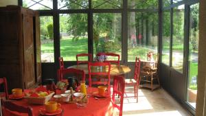 a dining room with a table with red chairs and a room with windows at Le Clos De La Roche in Goven