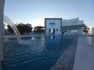 a swimming pool with a fountain in front of a house at Villa LINA Djerba Haut Standing in Aghīr
